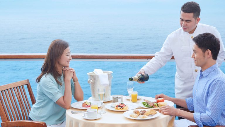 Couple enjoys Balcony Dining; server pours champagne