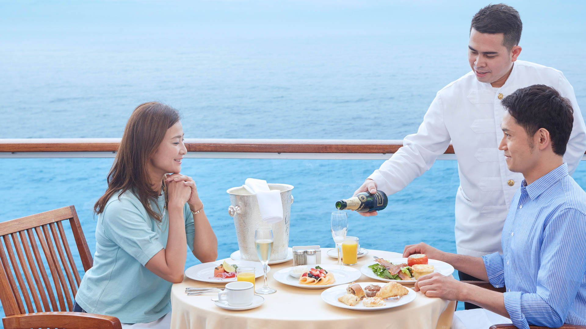 Couple enjoys Balcony Dining; server pours champagne