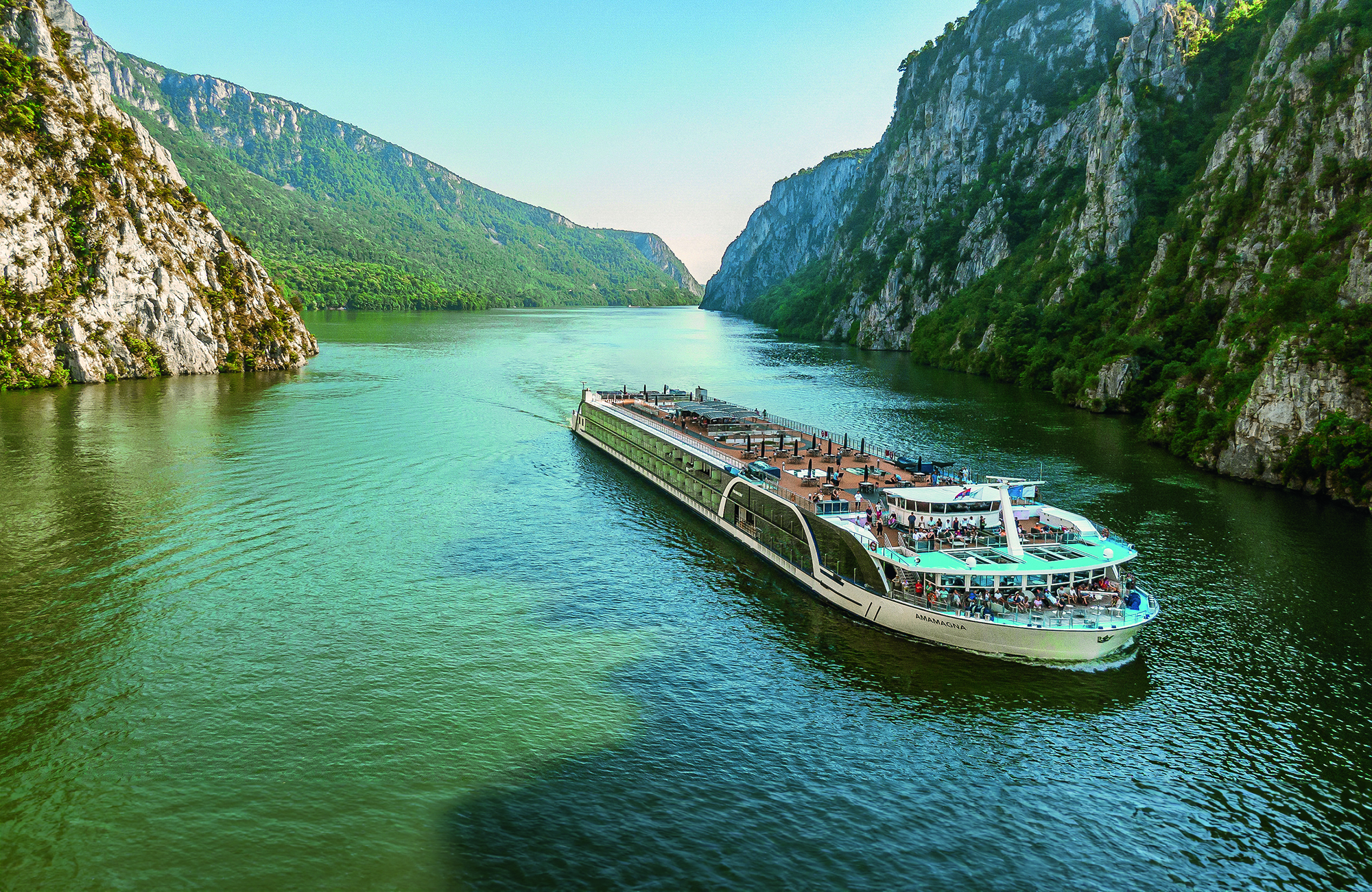 An exterior view of AmaMagna sailing through a gorge. It is twice the width of almost every other river ship in Europe.