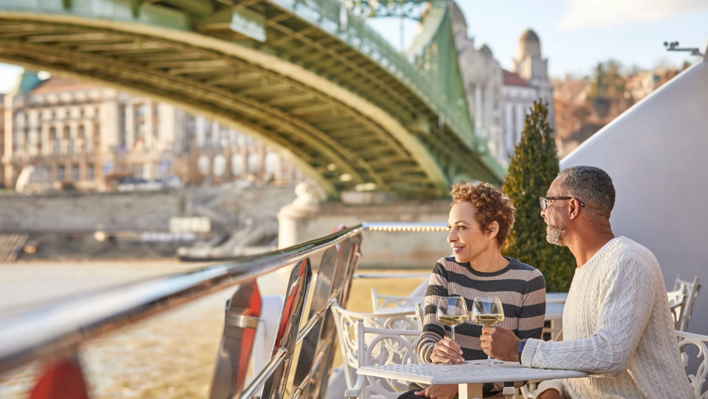 Uniworld couple sititng on a ship under a bridge in Europe