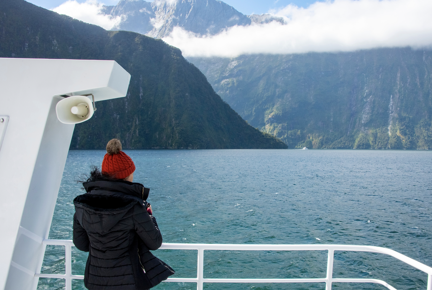 Woman looks off boat over Milford Sound landscape.